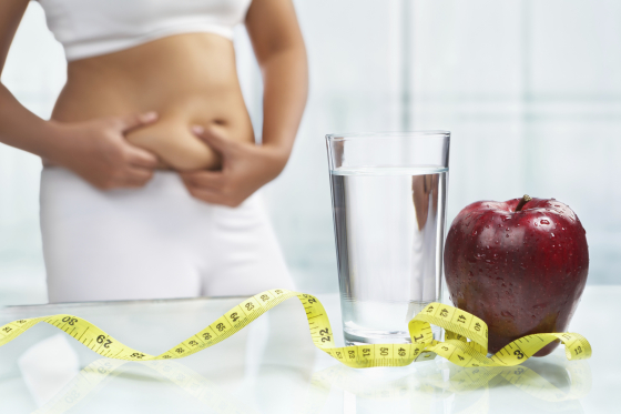 Women pinching waist behind a glass of water, apple and tap measure